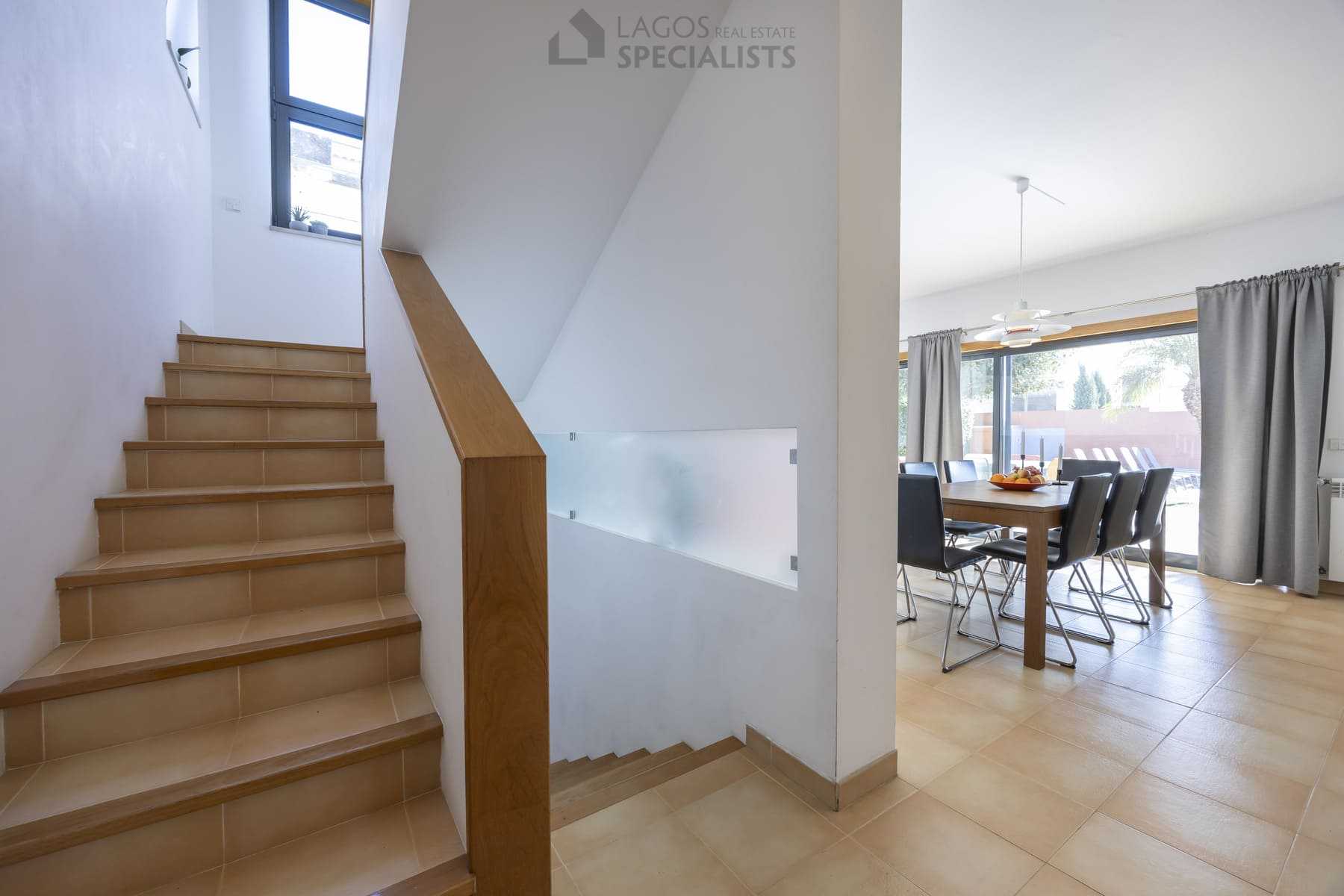 Staircase with wooden handrail leading to bright dining area, Lagos villa