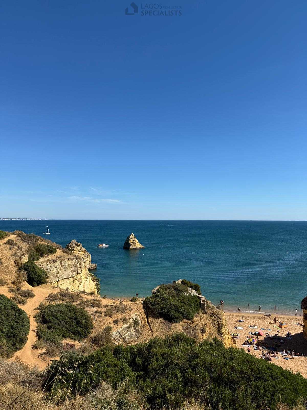 View of Praia Dona Ana in Lagos with golden cliffs, turquoise water, and boats in the distance