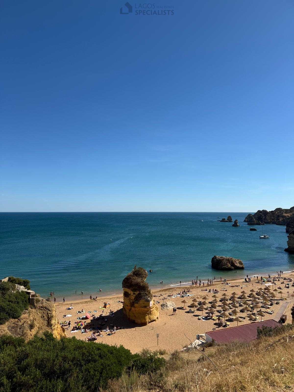 Sunny summer day at Praia Dona Ana, Lagos, with people relaxing on the sand and cliffs in the background