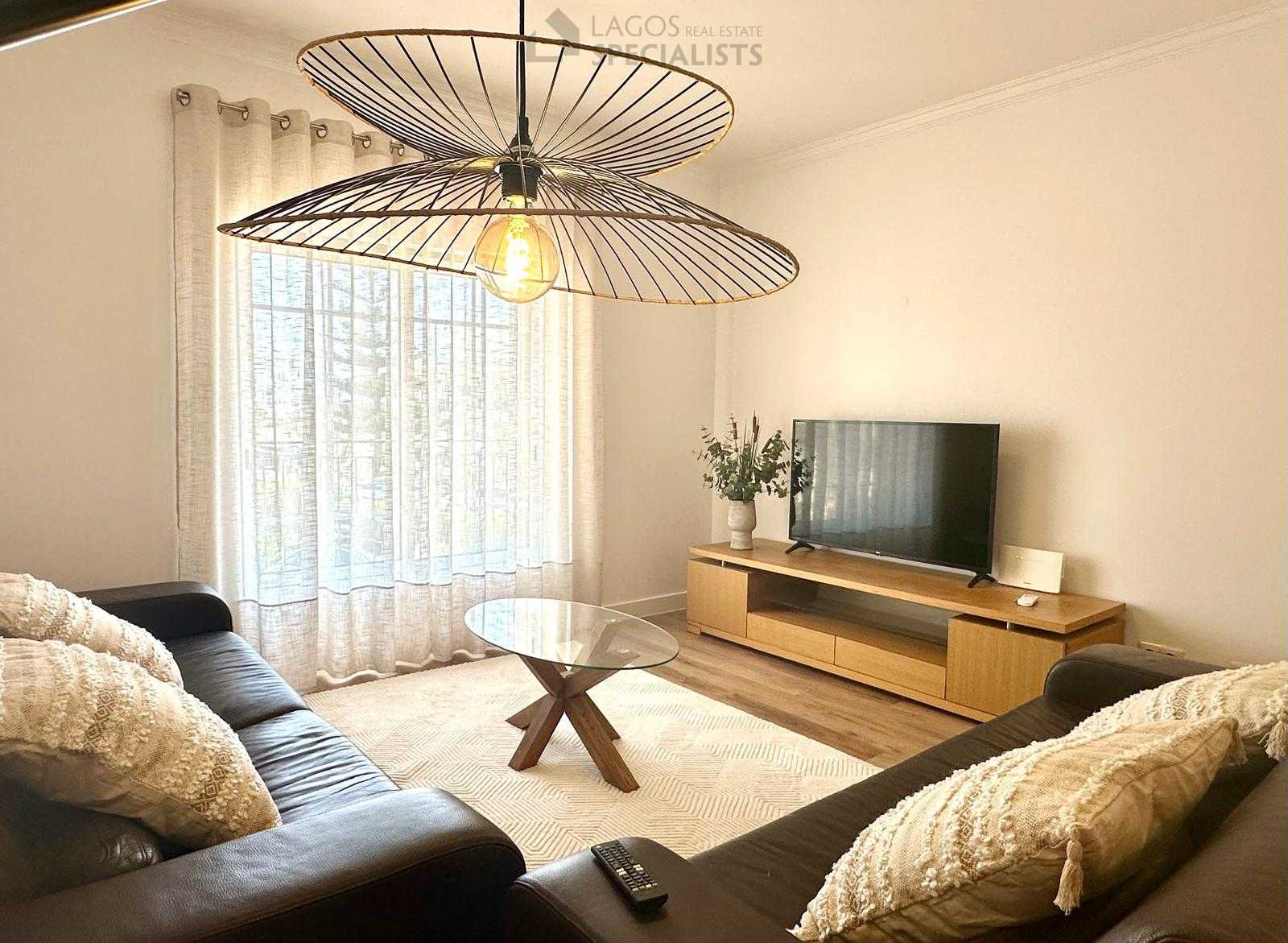 Modern living room with large window, sheer curtains, and stylish black sofas in Alporchinhos apartment