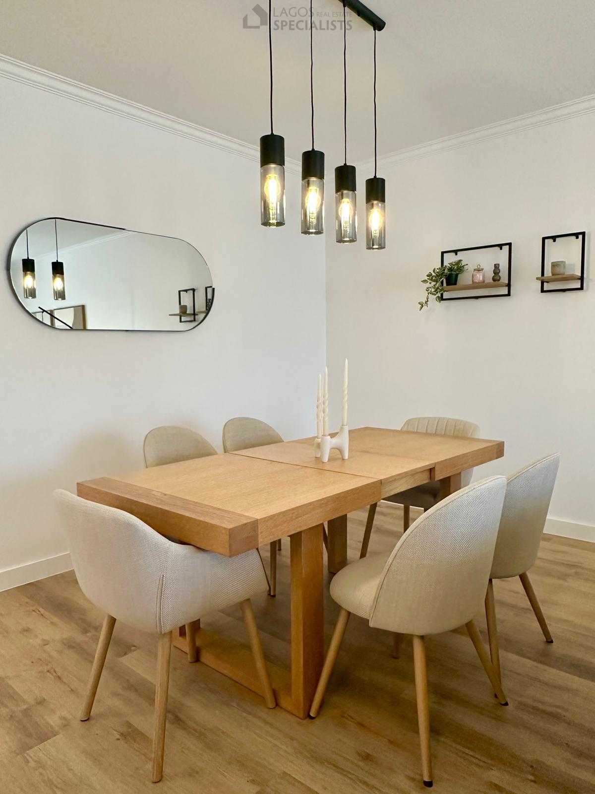 Open-plan dining and living area with wooden table, pendant lights, and soft neutral decor
