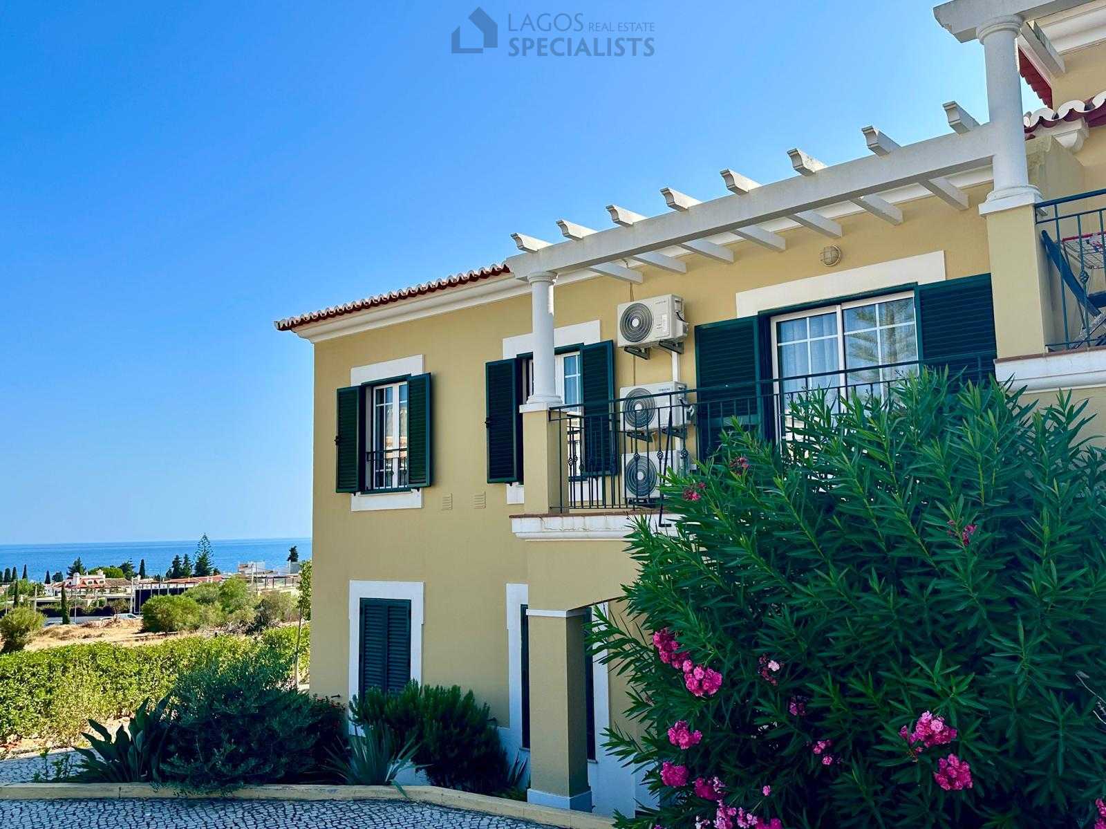 Exterior of yellow Algarve building with green shutters and pink flowers in bloom