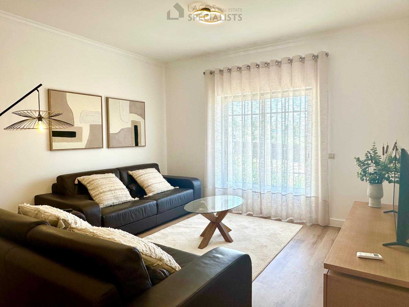 Modern living room with large window, sheer curtains, and stylish black sofas in Alporchinhos apartment