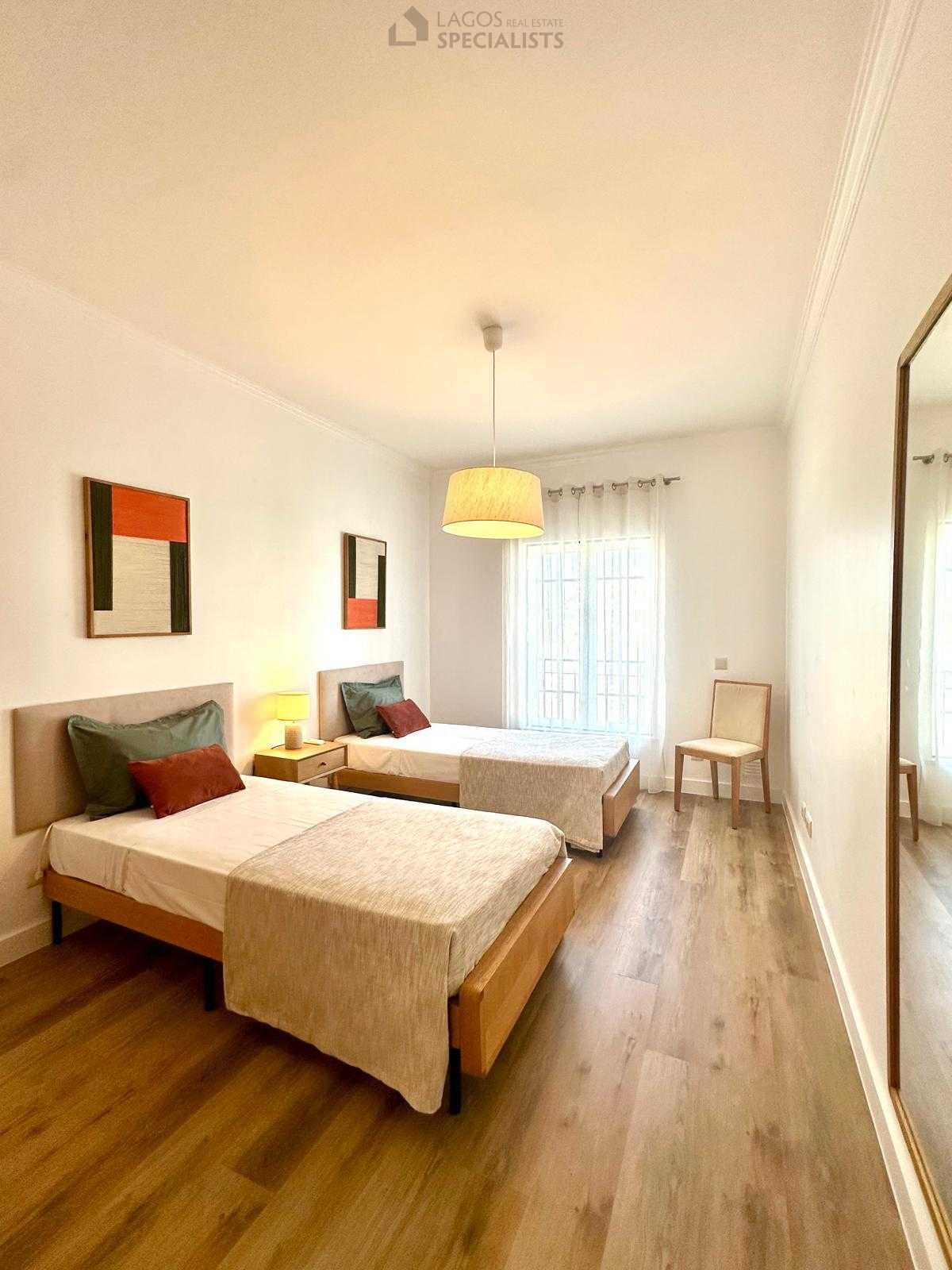 Twin bedroom with soft tones, wooden floor, and natural light from balcony window