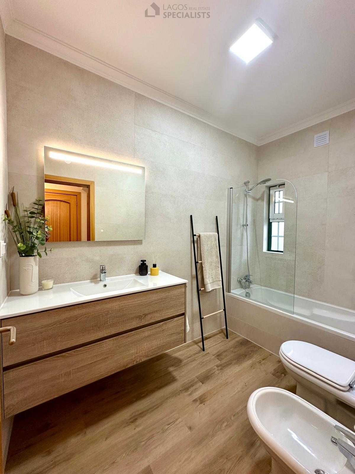 Contemporary bathroom with wooden vanity, neutral tiles, and soft lighting