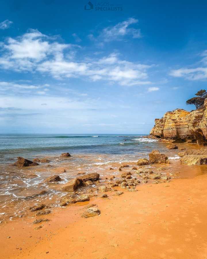 Golden Algarve beach with rocky cliffs and turquoise sea under a bright blue sky