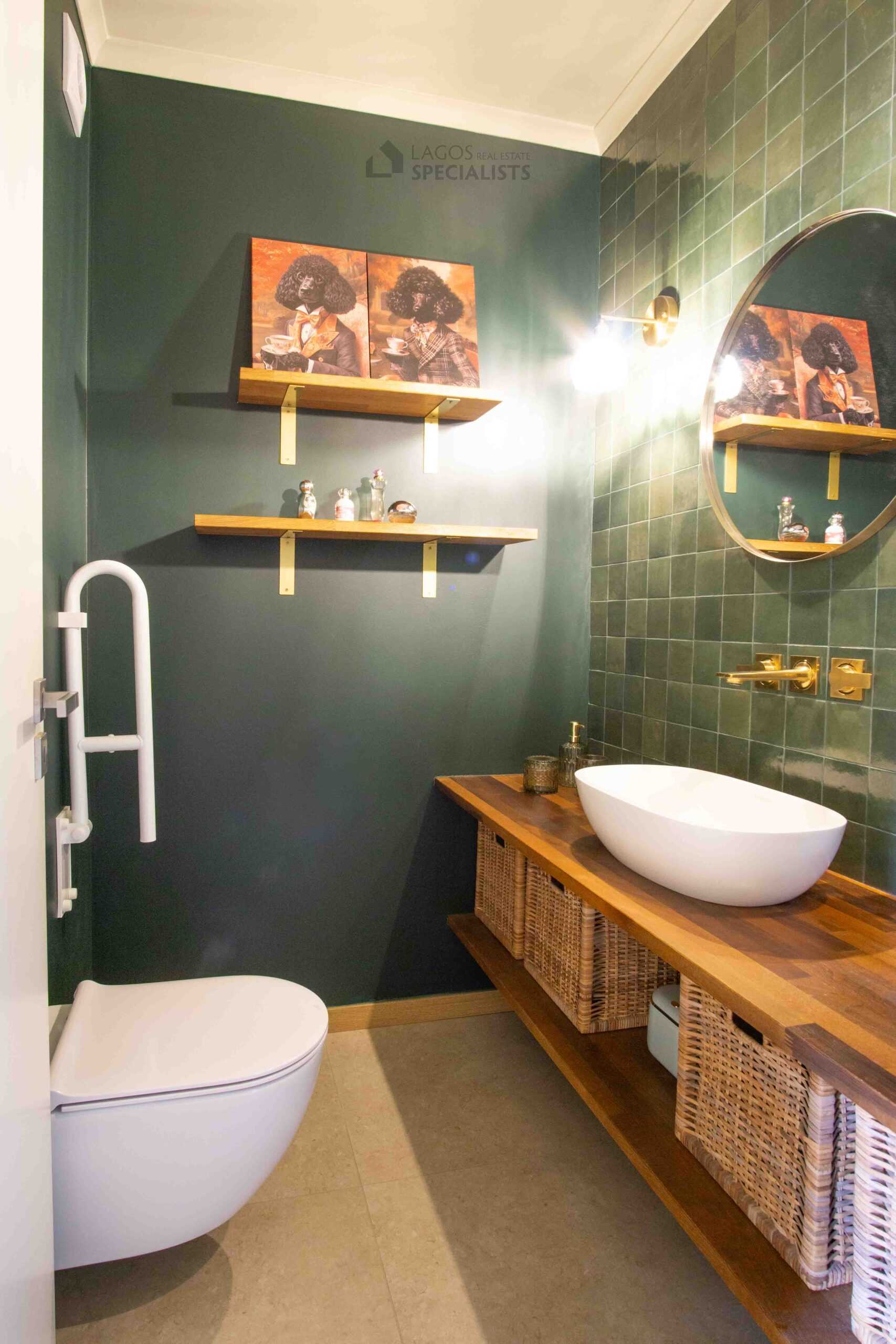 Modern guest bathroom with green tiled wall, wooden vanity unit, round mirror and warm lighting in Lagos apartment