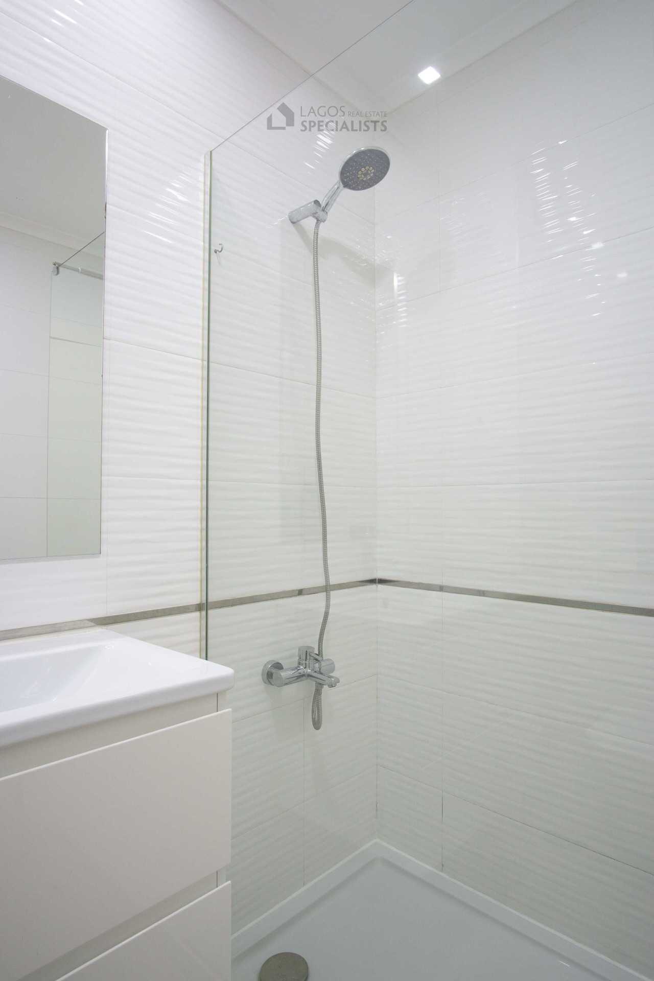 Minimalist walk-in shower with chrome fixtures, glass screen, and white tiled walls in a modern Lagos apartment bathroom