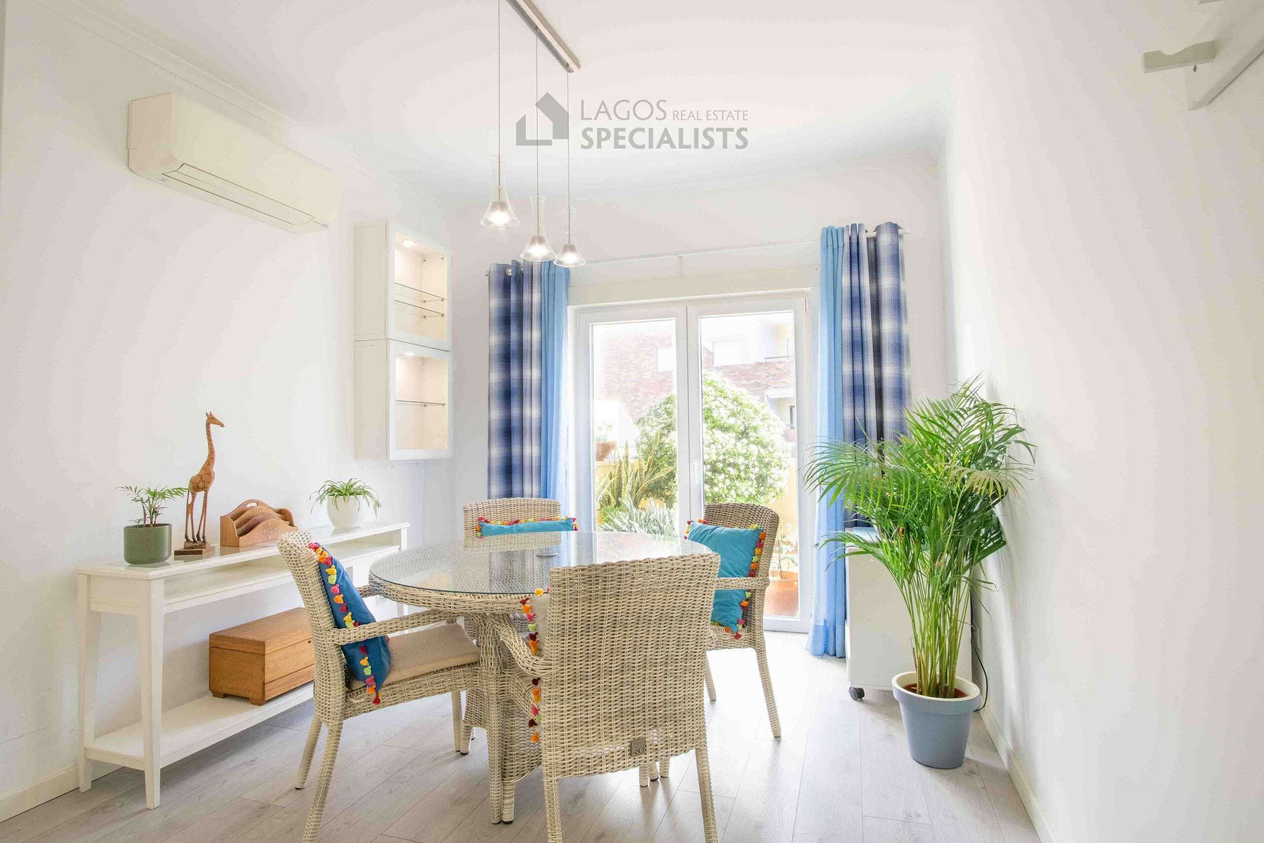 Bright dining area with wicker chairs, glass table, pendant lighting, and direct access to a private terrace in Lagos apartment