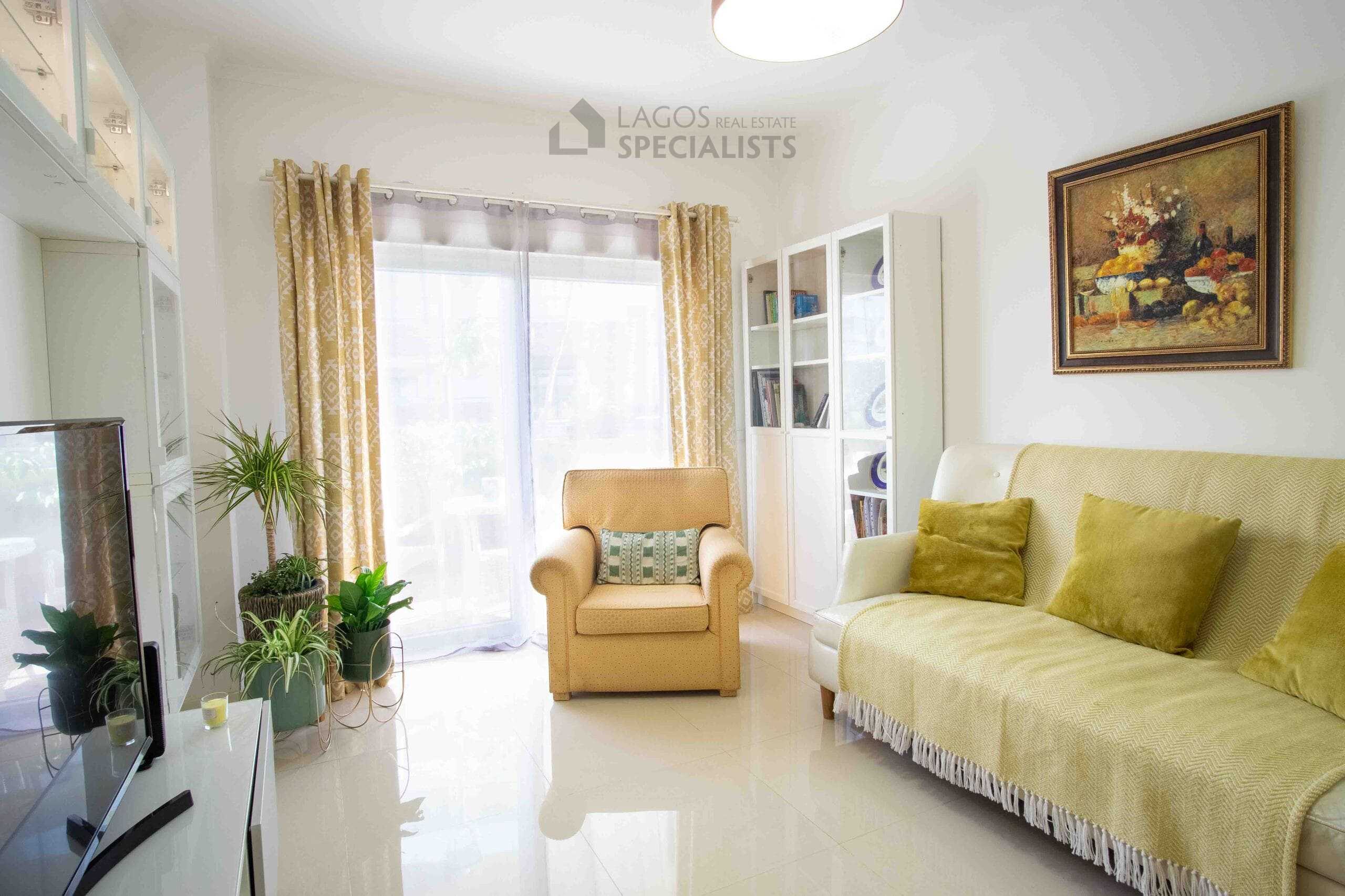 Living room seating area with armchair, sofa, indoor plants, and natural light