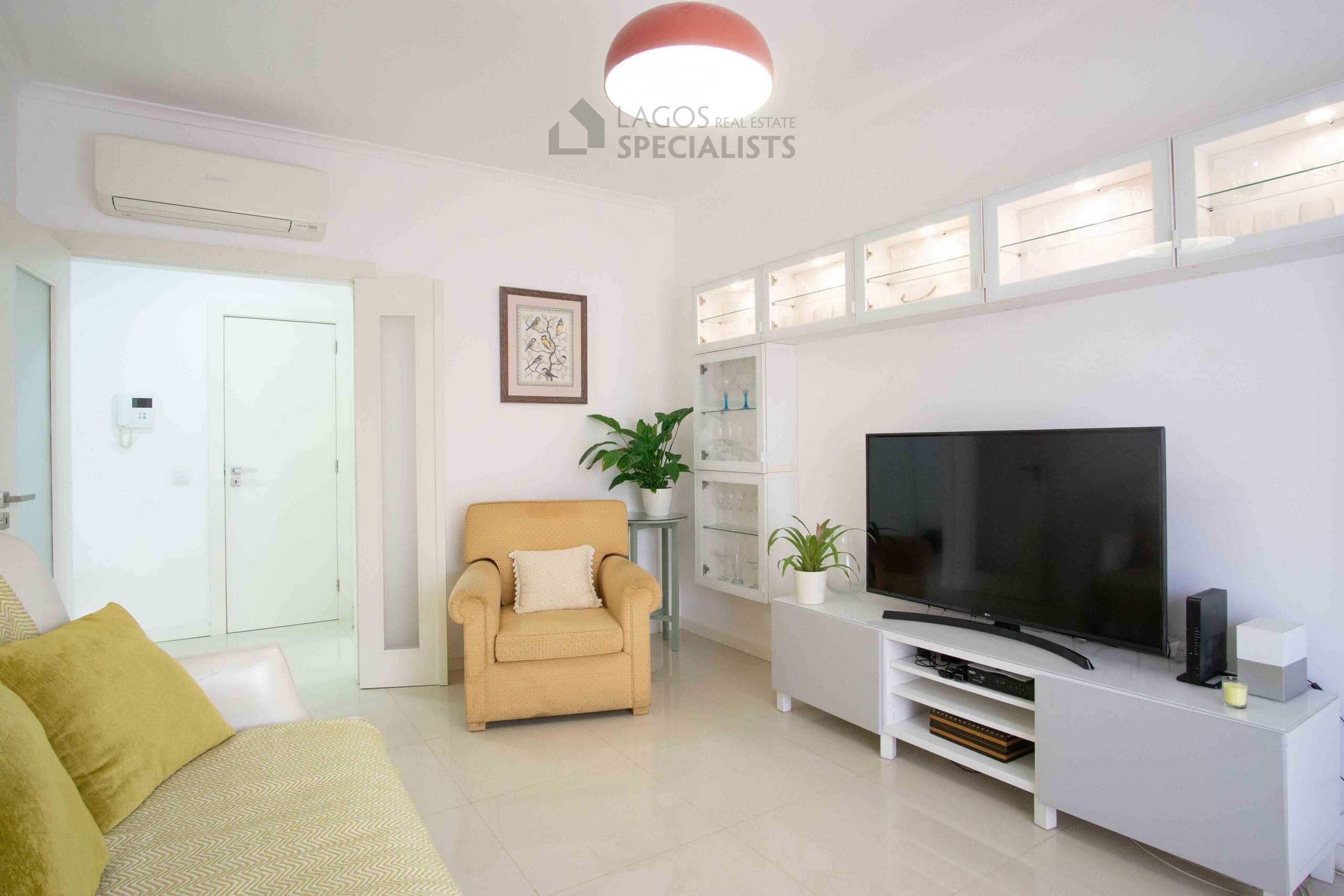 Living room with sofa, armchair, TV unit, and hallway leading to the rest of the apartment